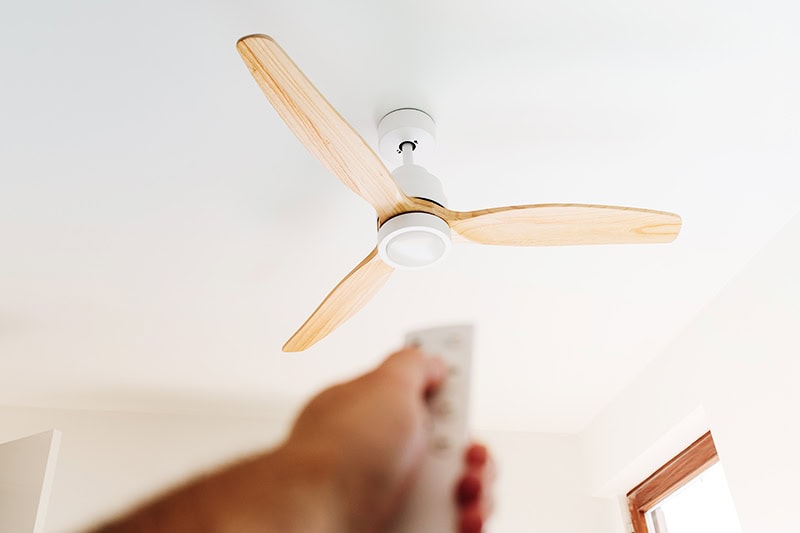 A person using a remote to turn on their ceiling fan