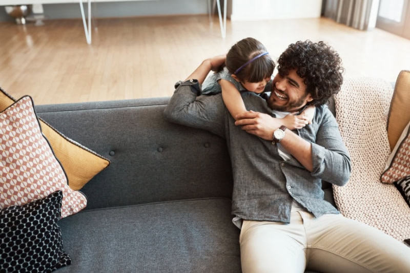 A father sitting on a couch while playing with his son