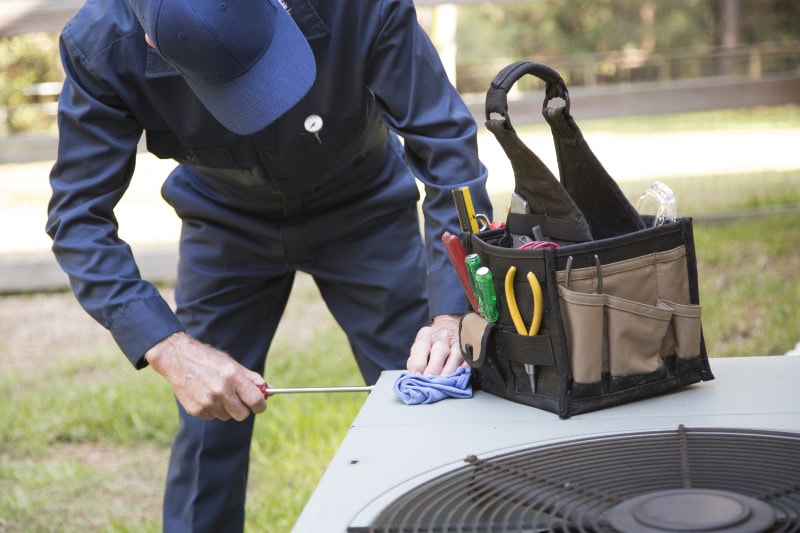 Technician performing maintenance on HVAC system, outside home in San Antonio, TX.